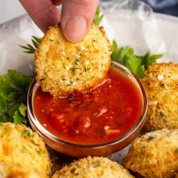 hand dunking air fryer fried ravioli in marinara sauce.