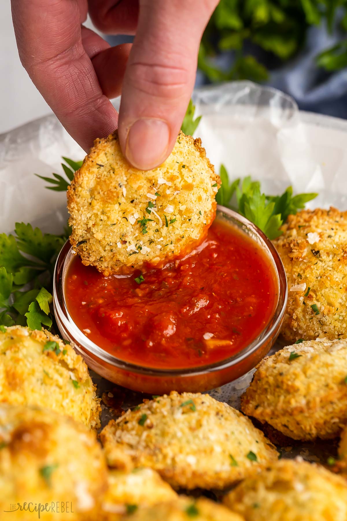 hand dunking air fryer fried ravioli in marinara sauce.