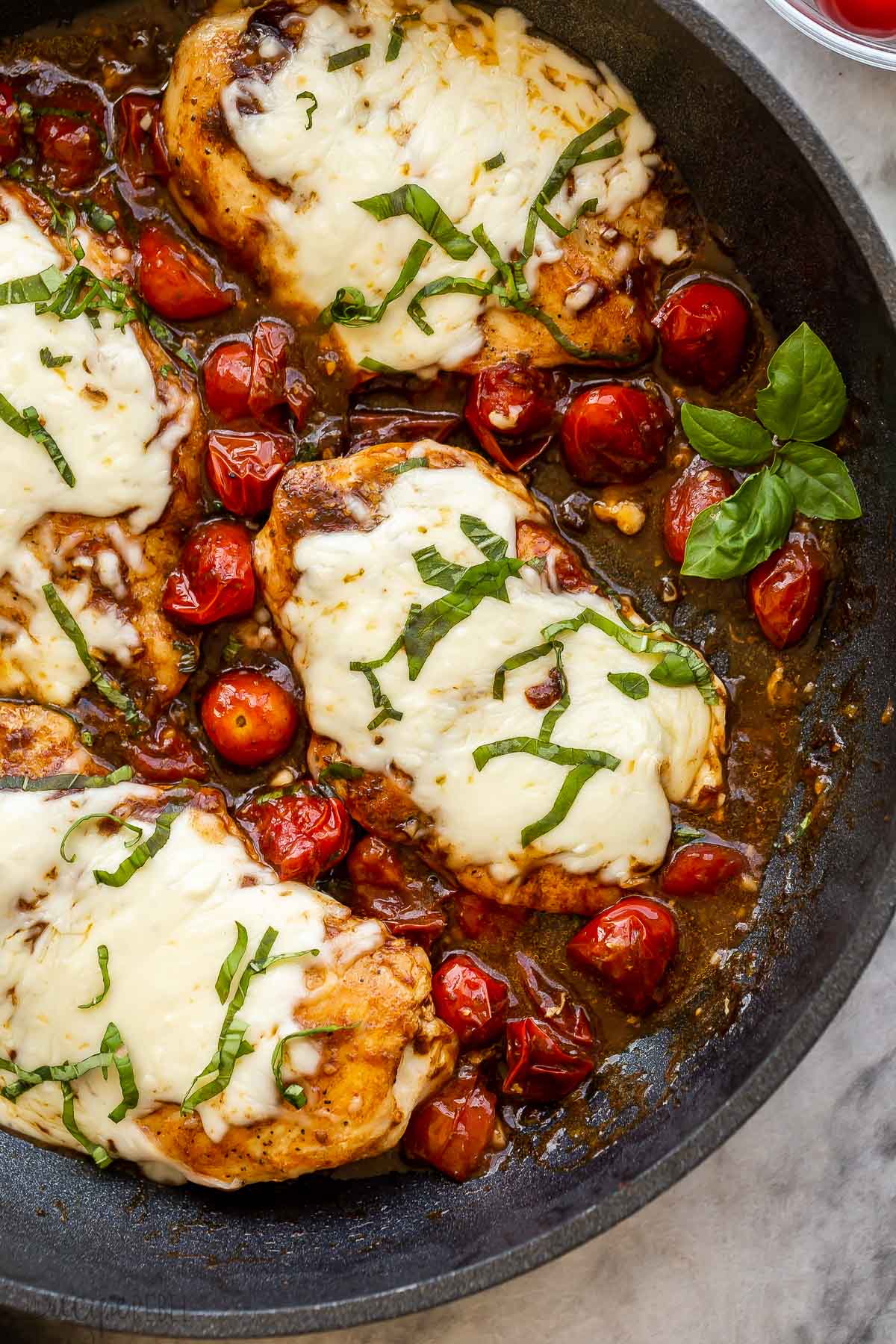 close up image of caprese chicken breast topped with mozzarella and basil.
