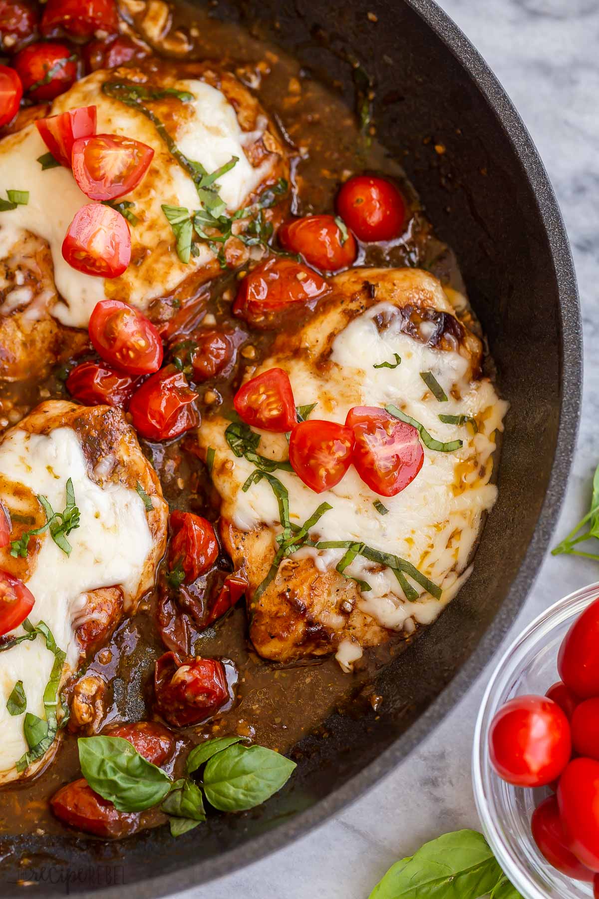 close up image of chicken caprese in black skillet with fresh tomatoes.