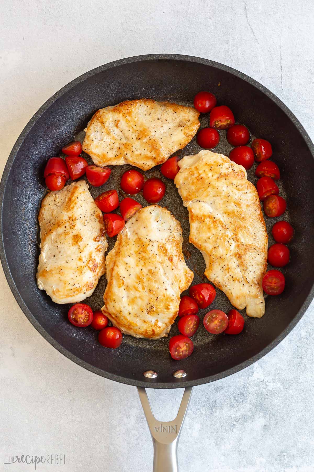 browned chicken breasts in skillet with cherry tomatoes.