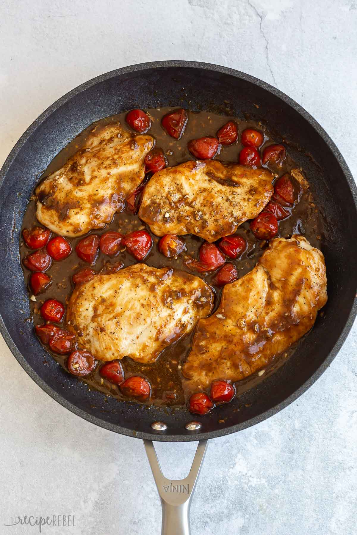 chicken breasts tomatoes and sauce in black skillet.