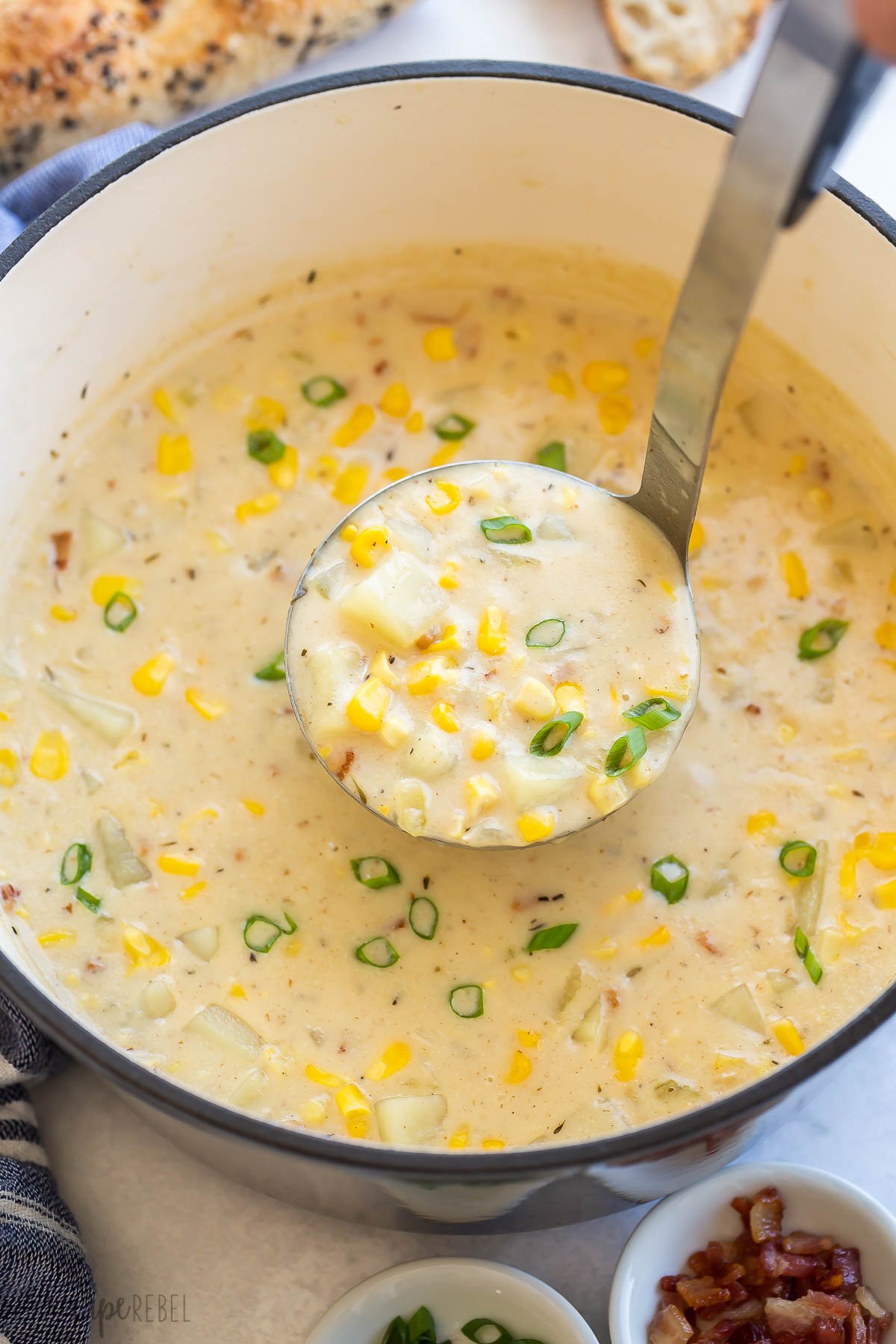 metal ladle scooping potato corn chowder from dutch oven.