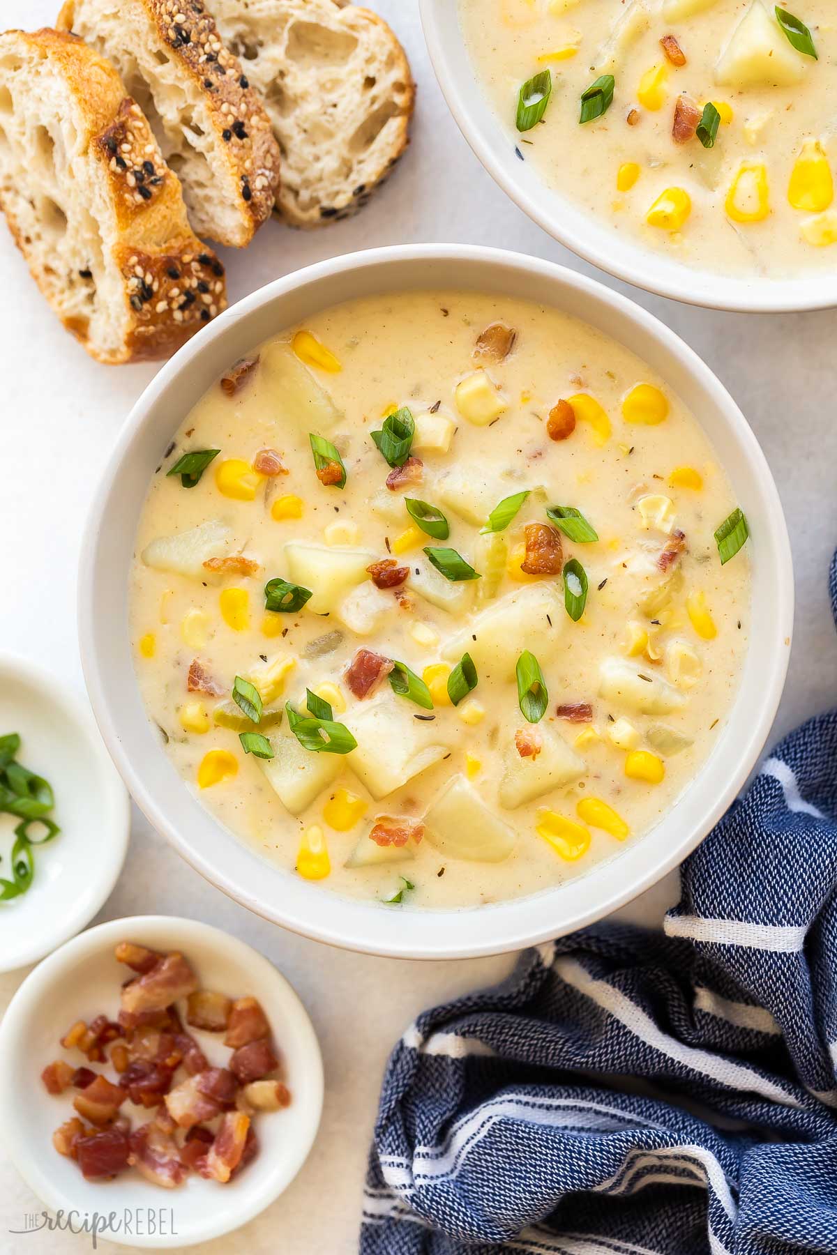 bowl of corn chowder with bacon pieces green onions and bread on the side.