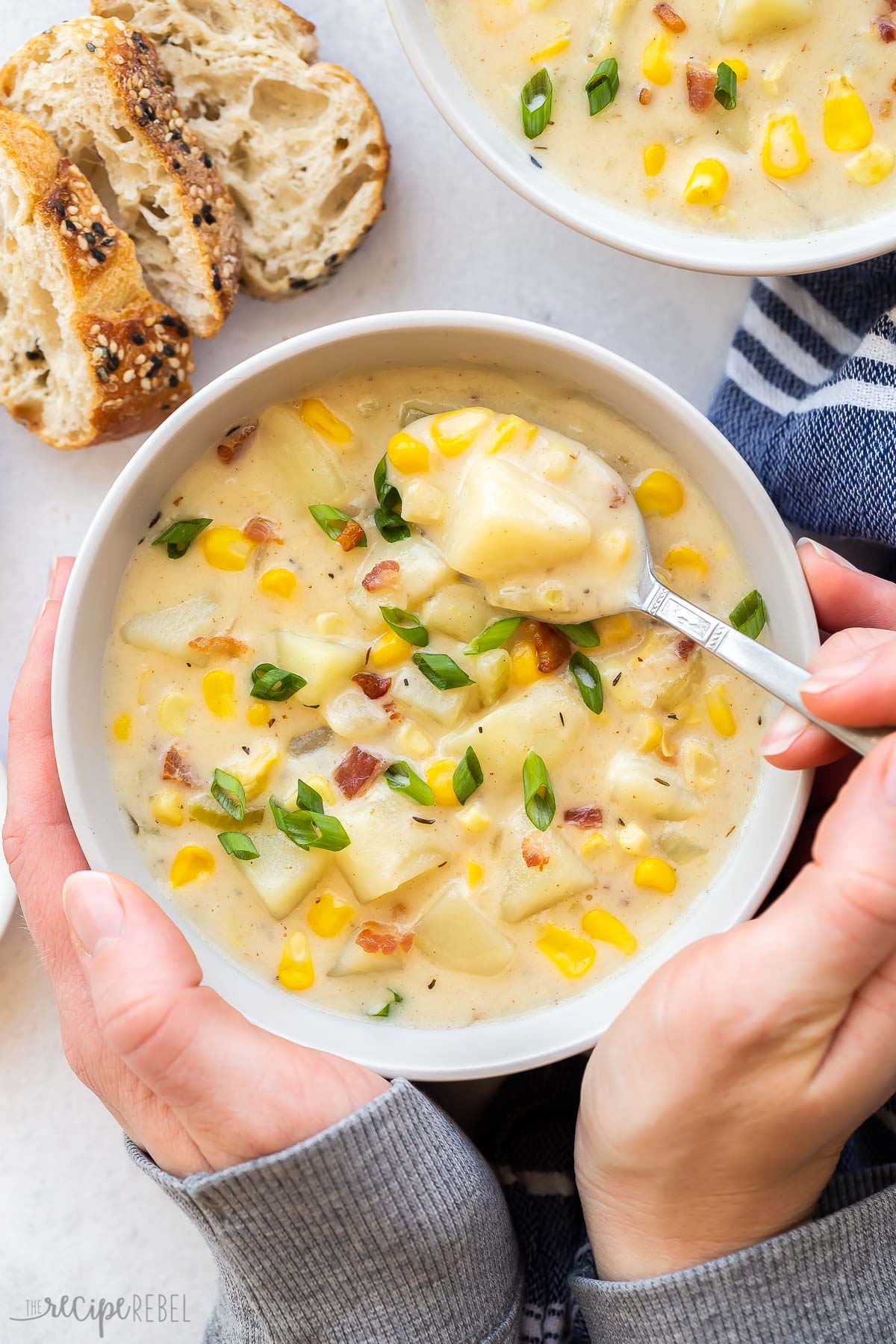 two hands holding bowl of potato corn chowder with spoon.