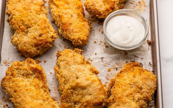 square image of crispy baked chicken strips on a sheet pan with parchment.