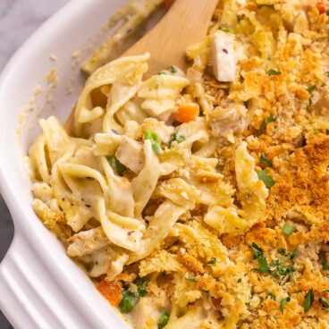 close up image of wooden spoon stuck in chicken noodle casserole.