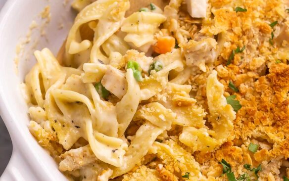 close up image of wooden spoon stuck in chicken noodle casserole.