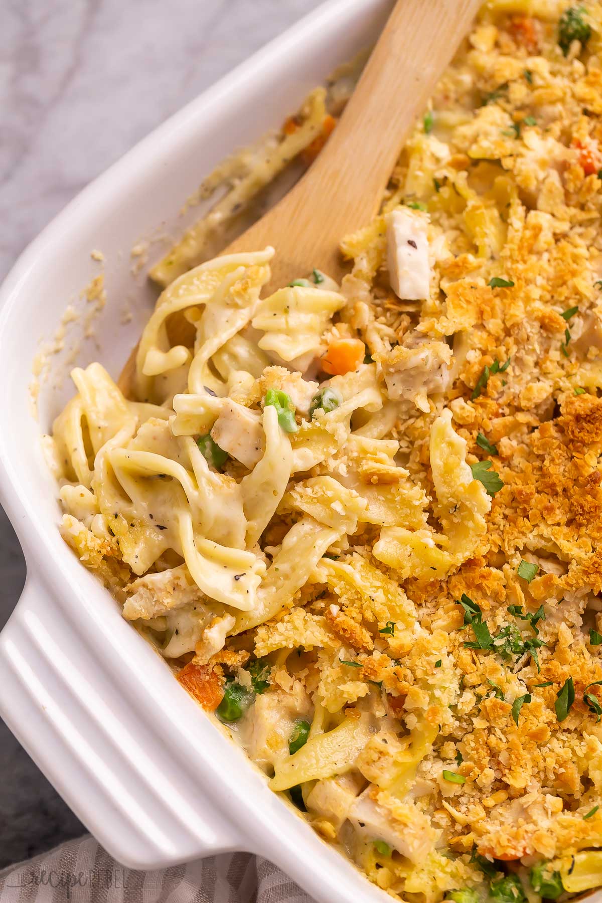 close up image of wooden spoon stuck in chicken noodle casserole.