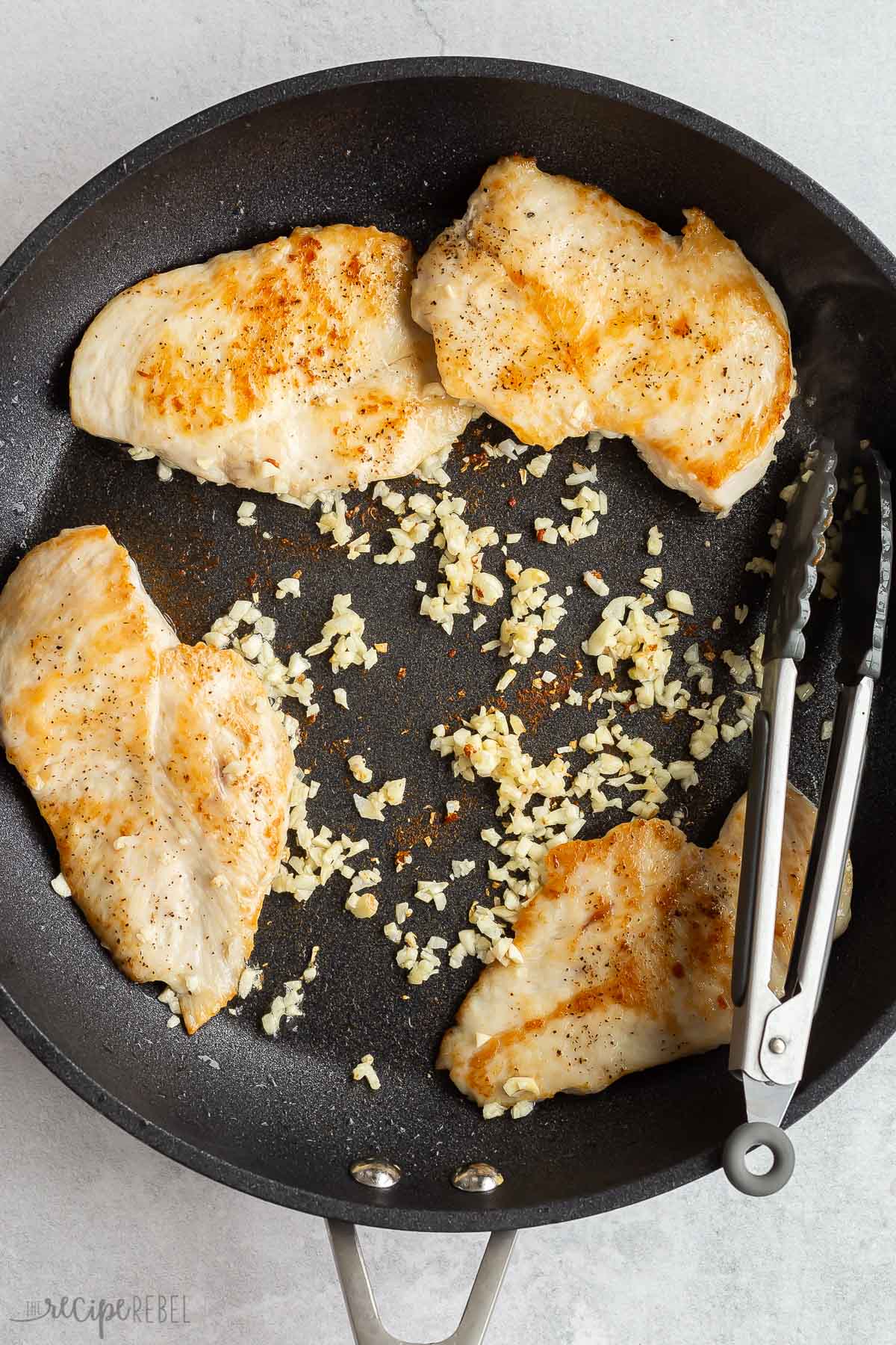 garlic and spices added to chicken breasts in skill.et
