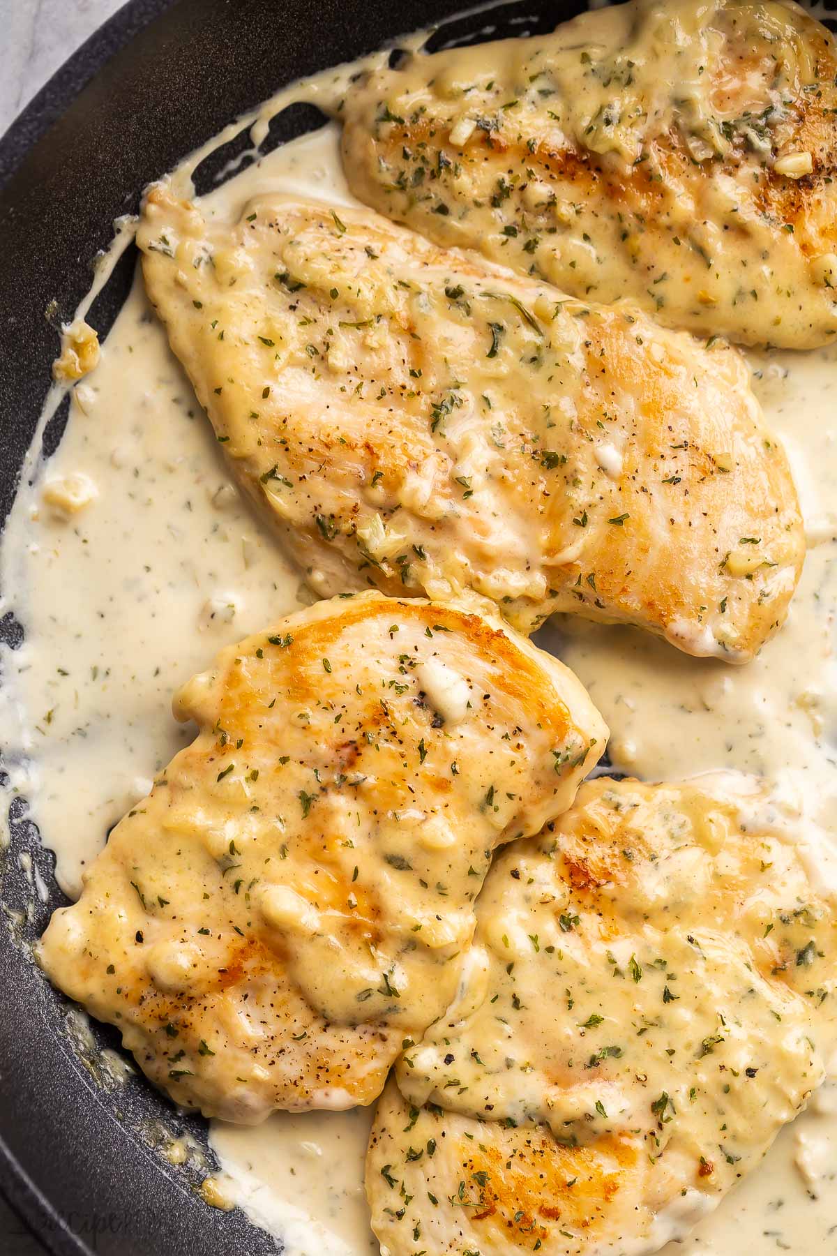 close up image of four creamy garlic chicken breasts in black skillet.