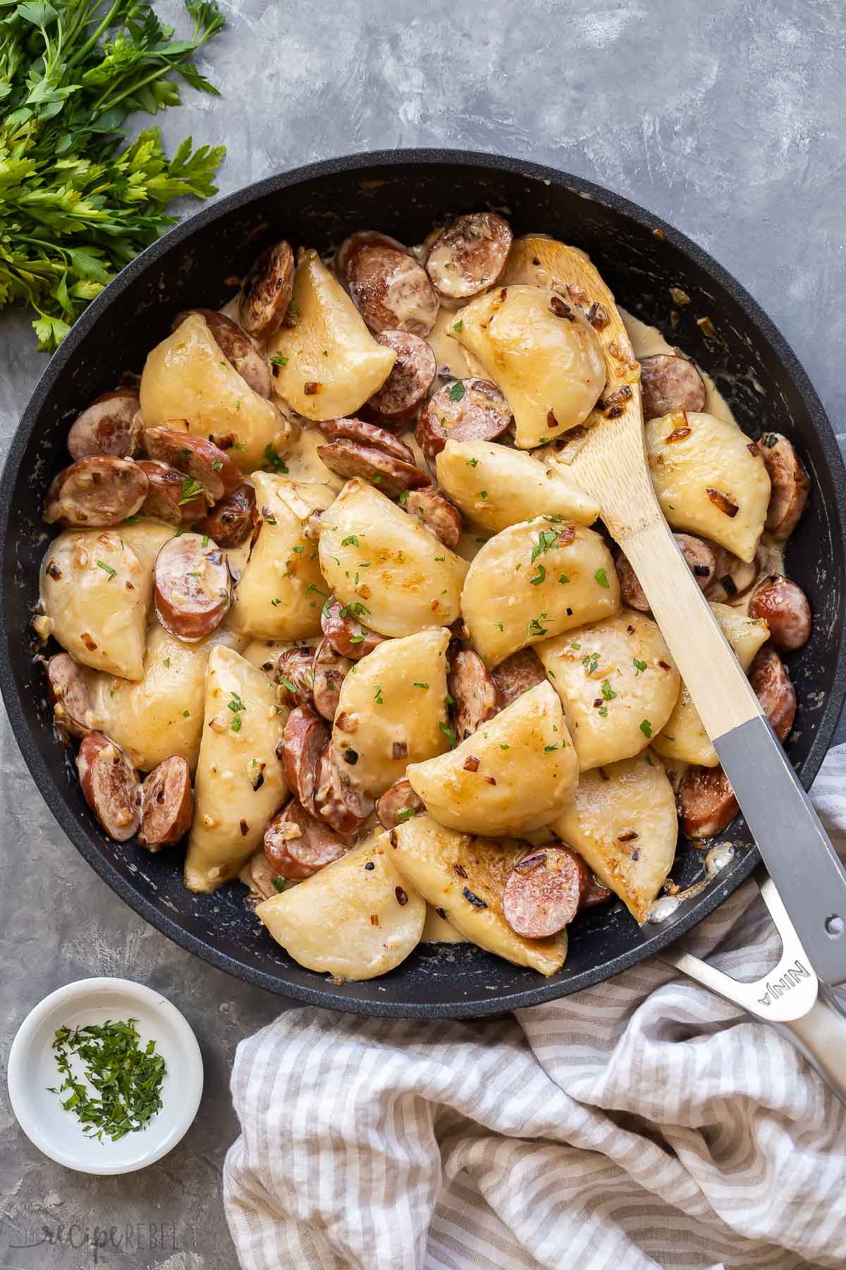 overhead image of perogies and sausage in black skillet on grey background.