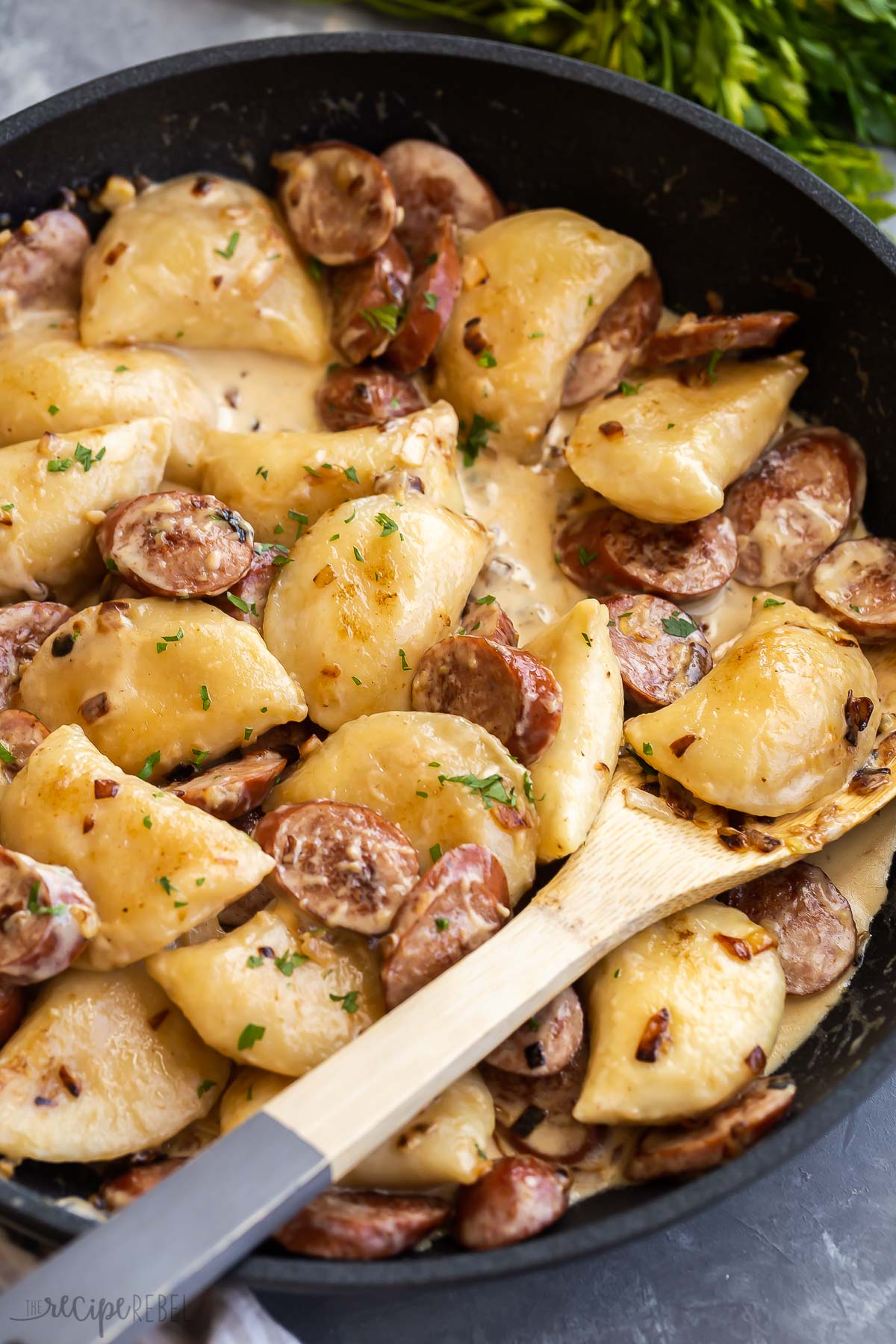 close up image of pierogis and sausage in skillet with wooden spoon.