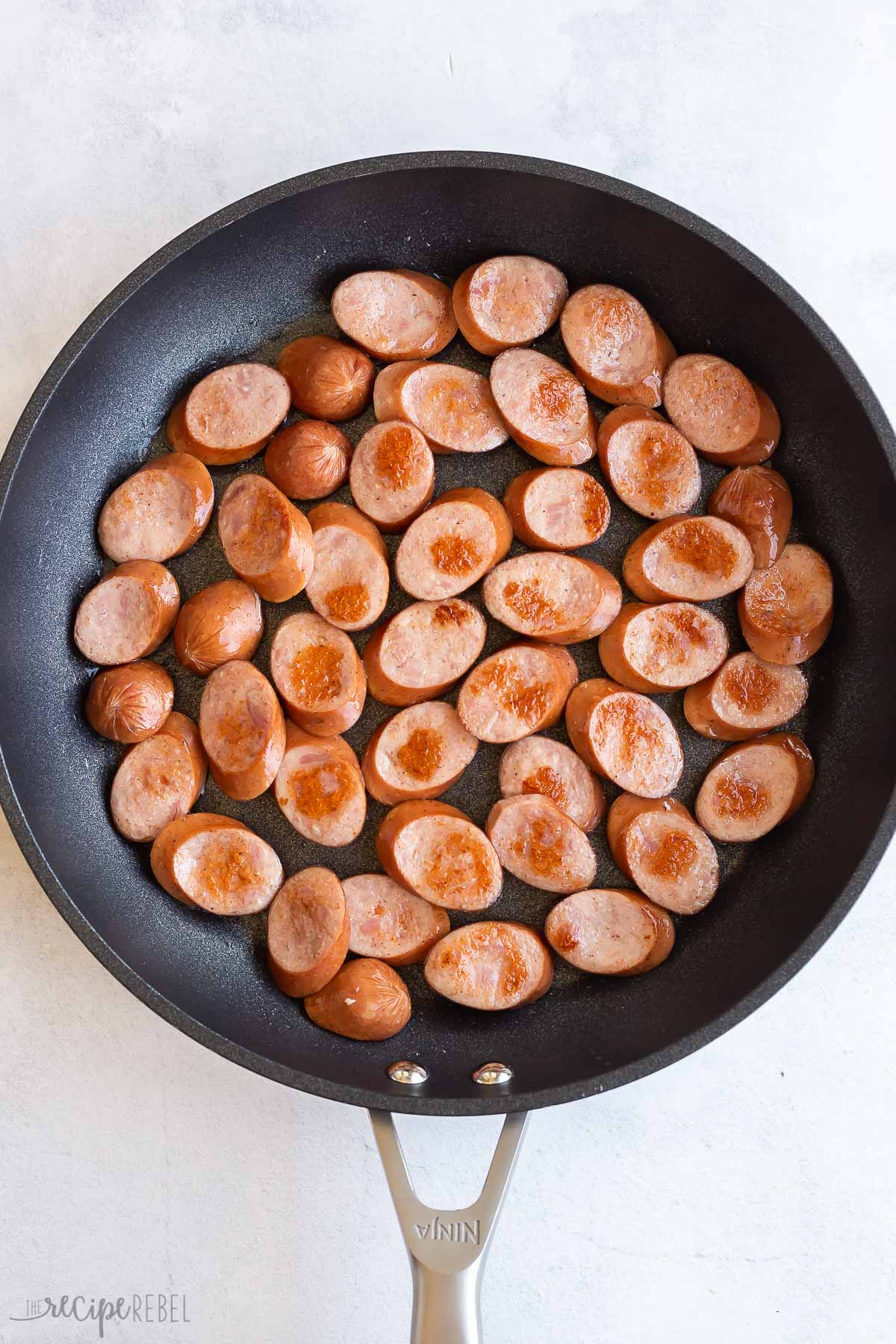 slices of smoked sausage browning in black skillet.