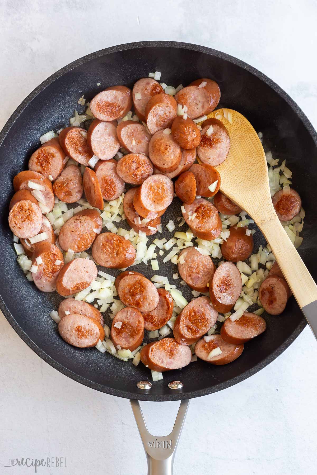 onion added to smoked sausage in skillet.