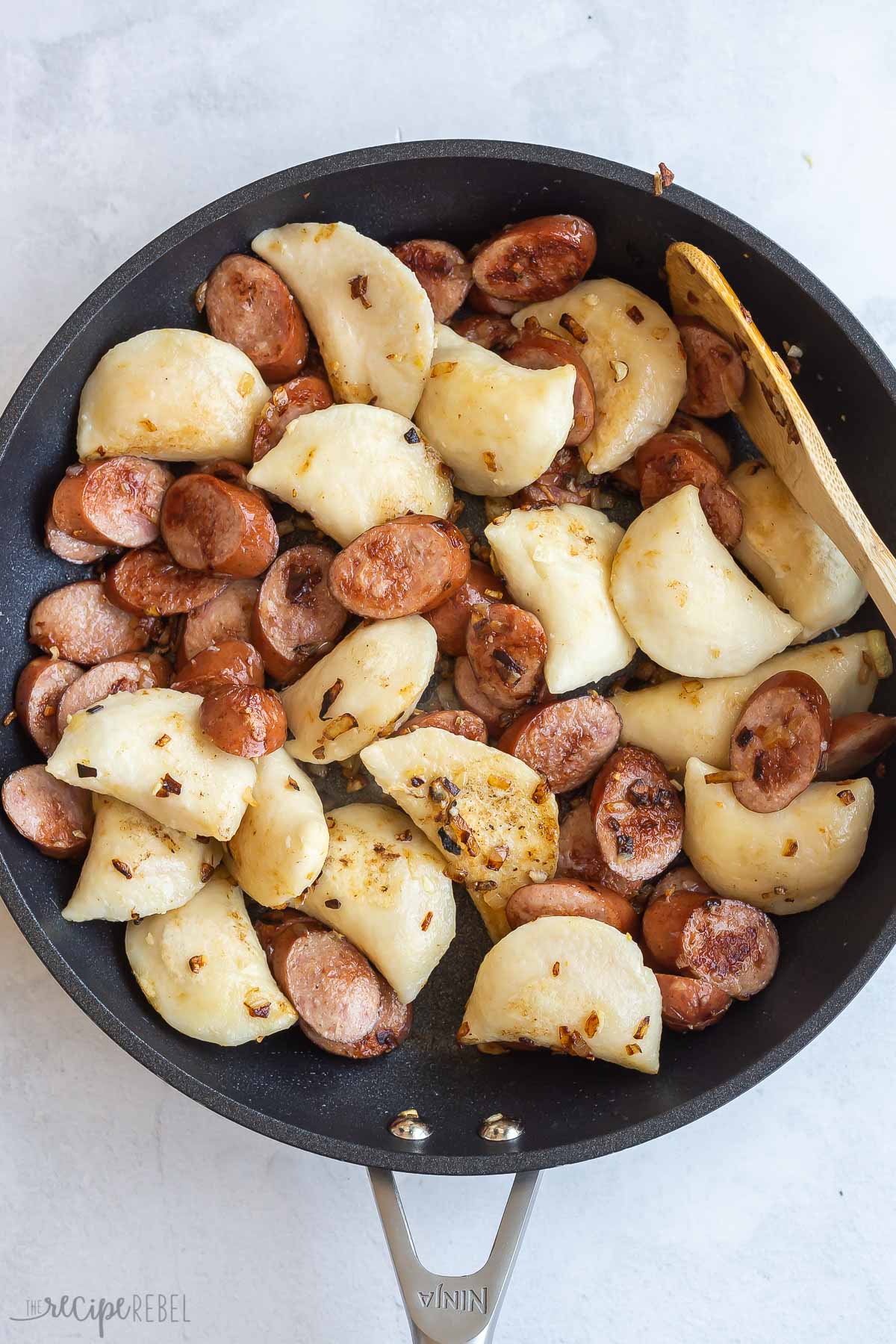 cooked pierogi added to sausage in skillet.