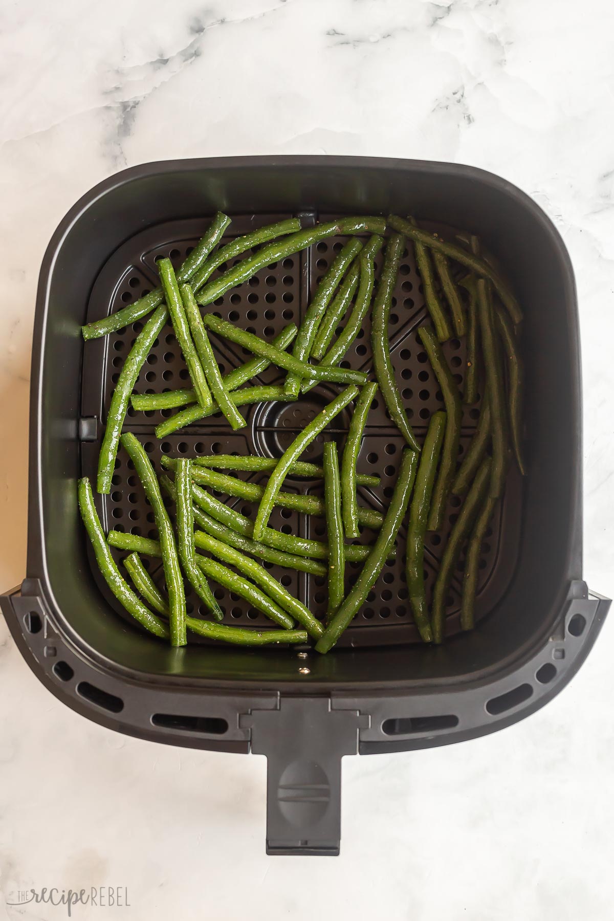 seasoned green beans in air fryer basket ready to cook.