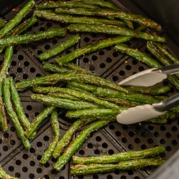 tongs picking up roasted green beans from air fryer.
