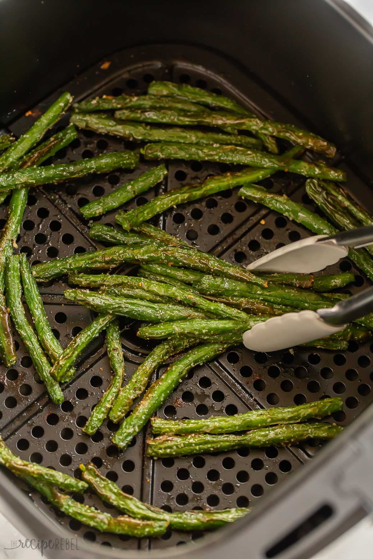 tongs picking up roasted green beans from air fryer.