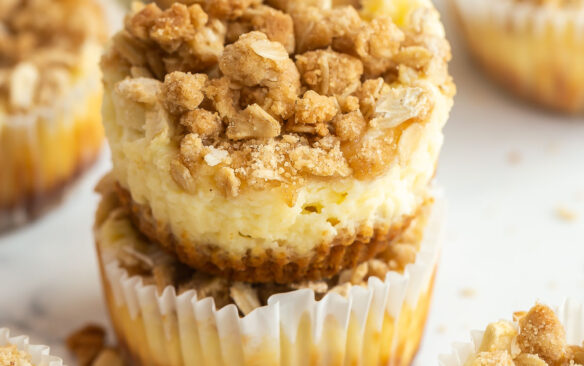 two apple crisp cheesecakes stacked with more in the background.