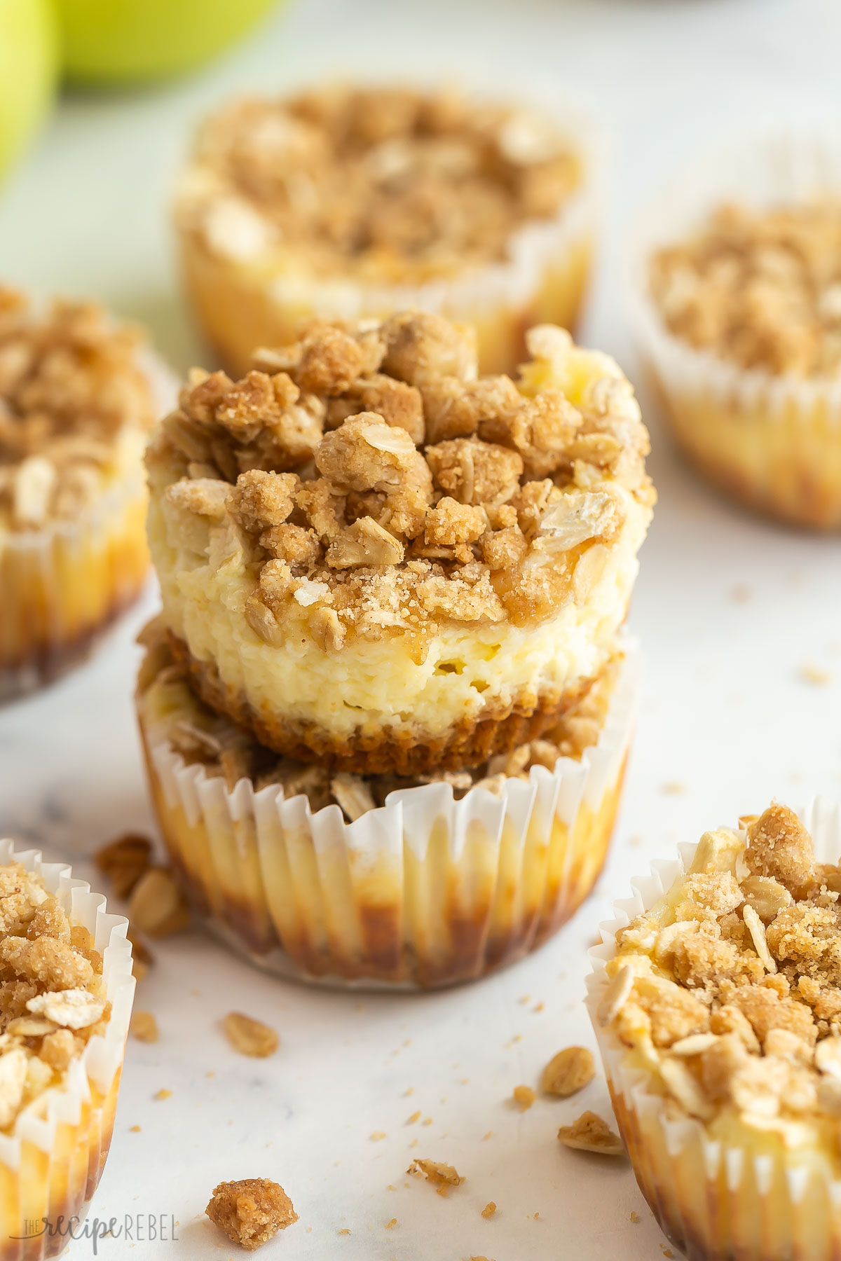 two apple crisp cheesecakes stacked with more in the background.