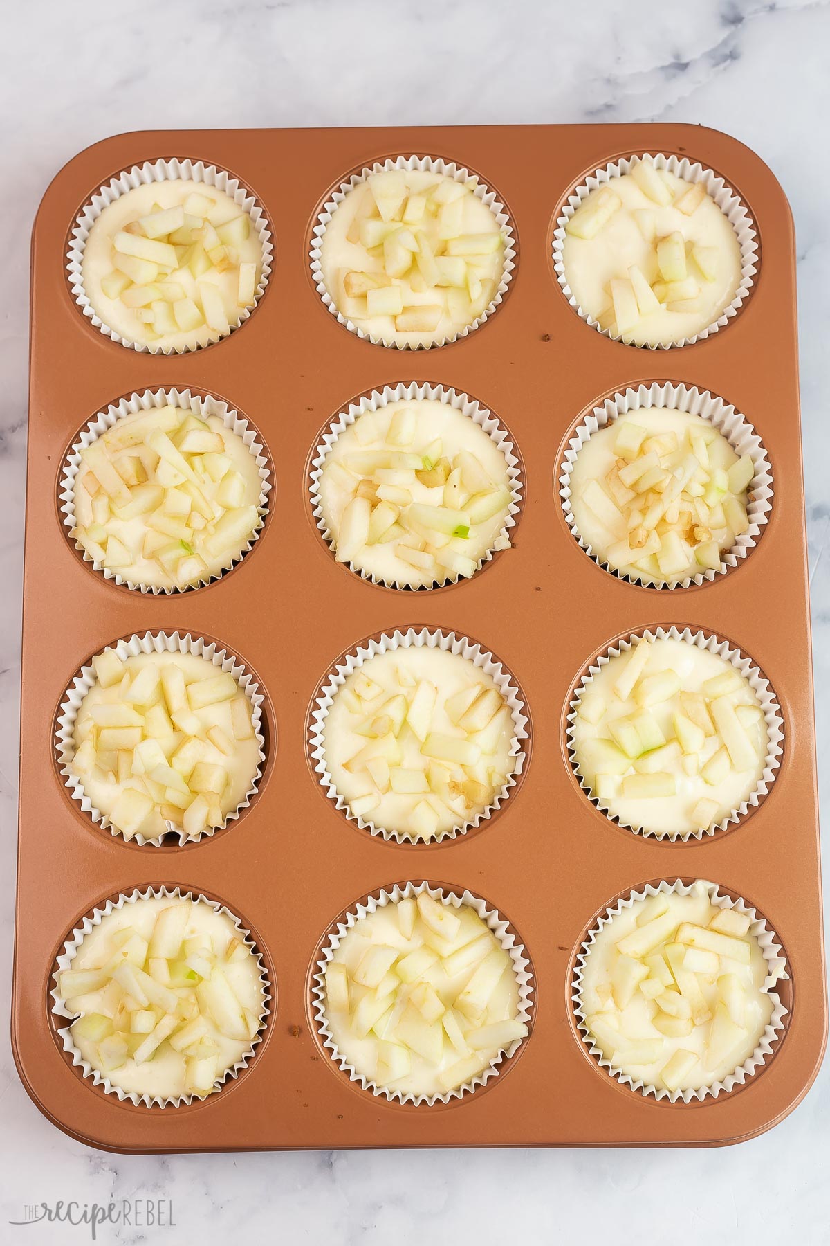 mini cheesecakes topped with apples in muffin pan.