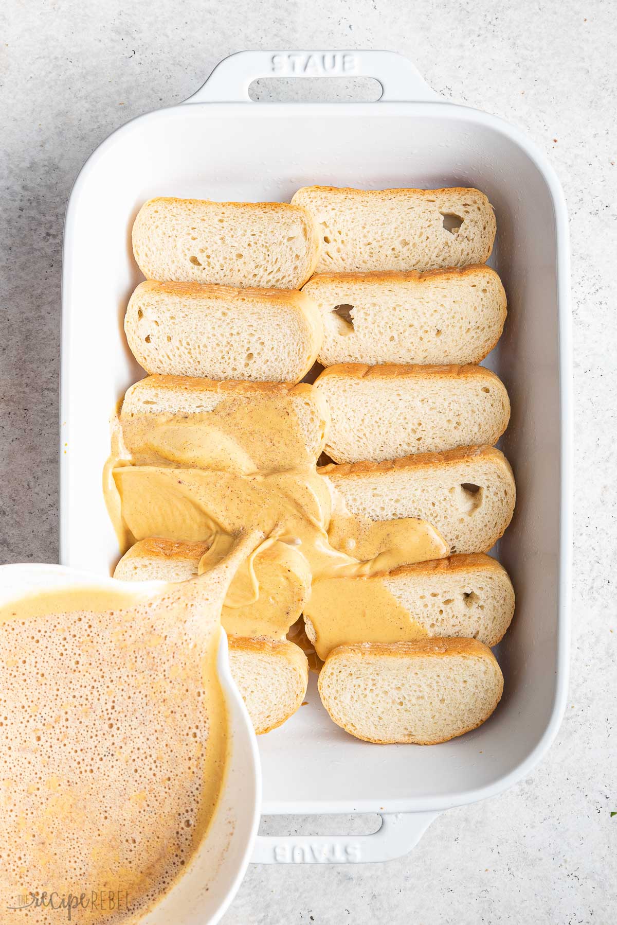 french toast batter being poured over bread in baking dish.