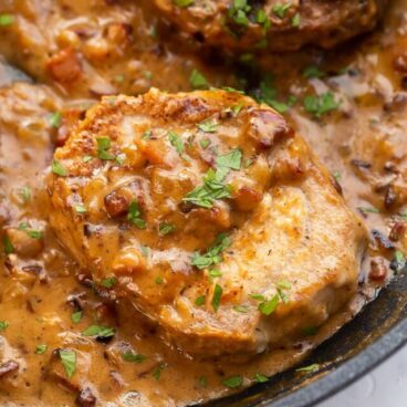 close up image of one pork chop with gravy and bacon.