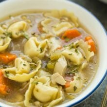 close up image of chicken tortellini soup in white bowl on grey background.