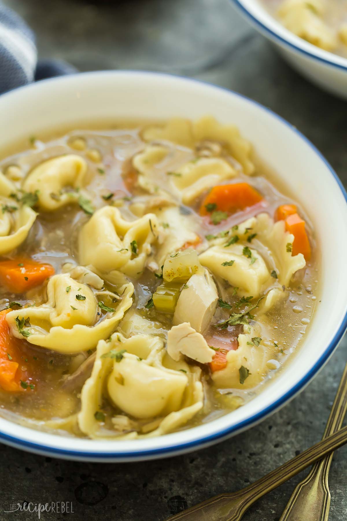 close up image of chicken tortellini soup in white bowl on grey background.