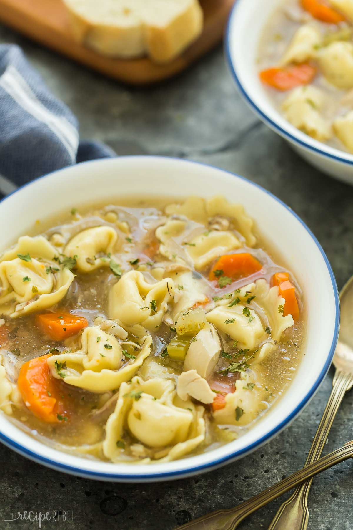 chicken tortellini soup in white bowl with blue rim.