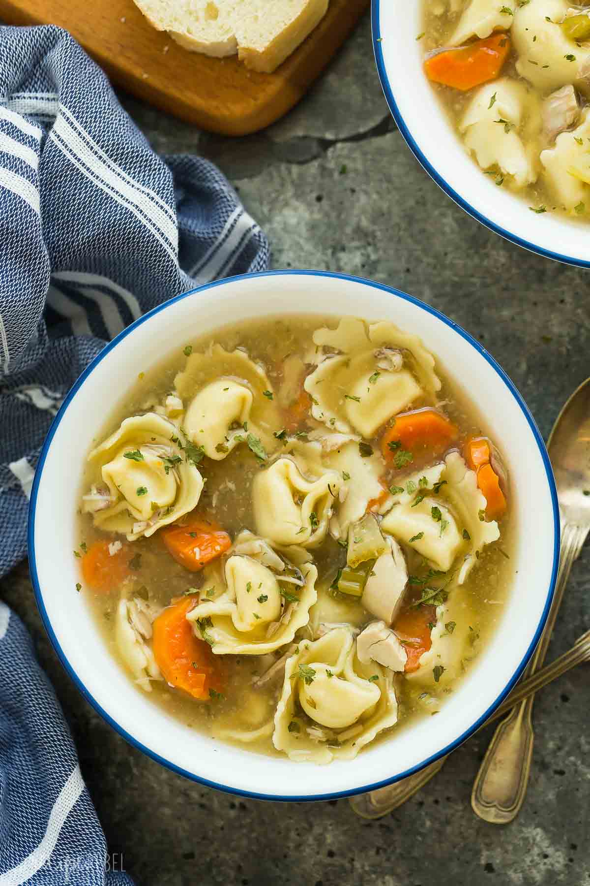 overhead image of white bowl of chicken tortellini soup on grey background.