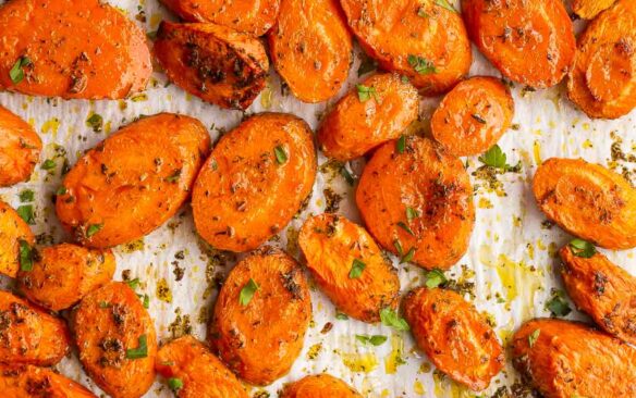 overhead image of roasted sliced carrots on parchment lined baking sheet.