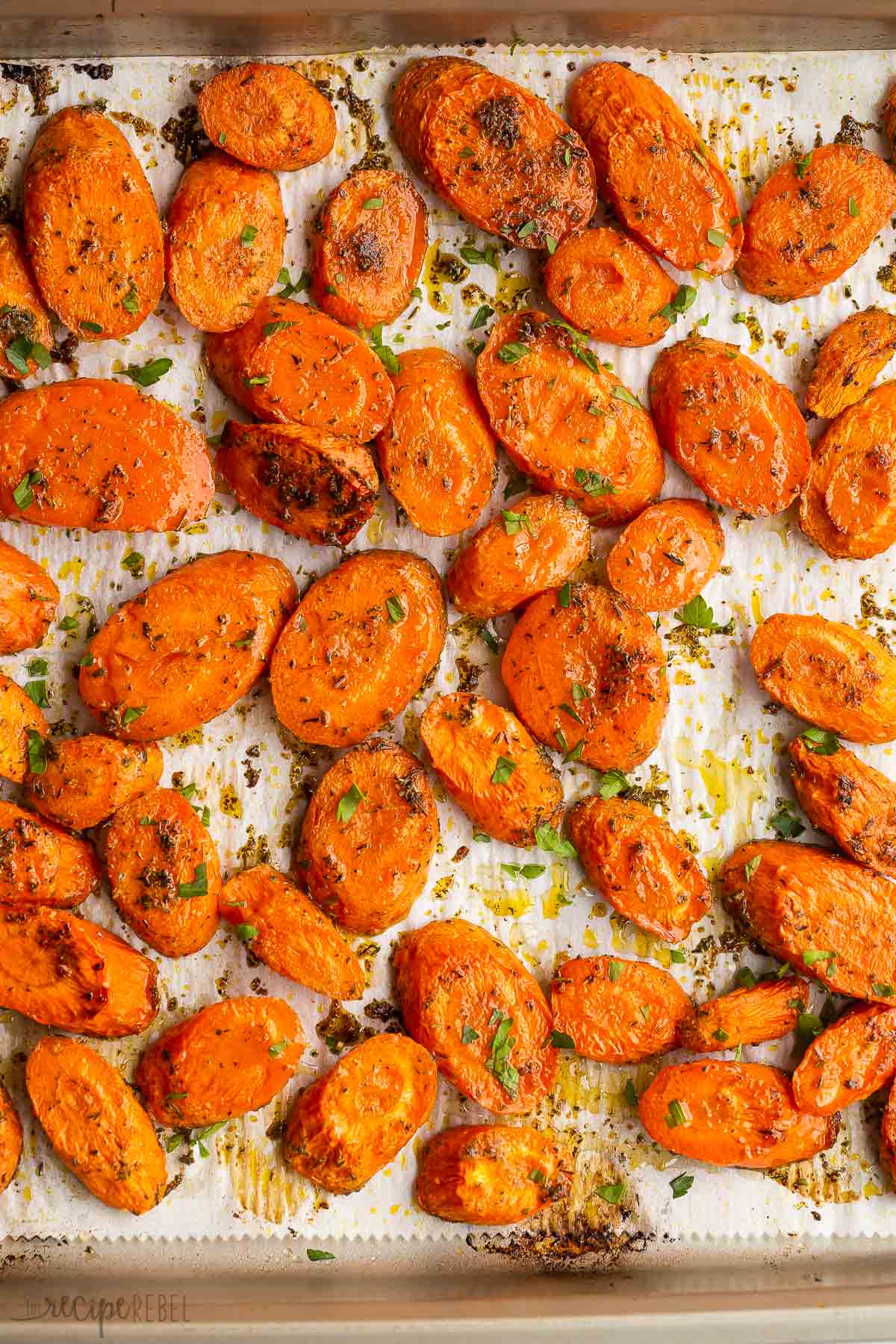 overhead image of roasted sliced carrots on parchment lined baking sheet.