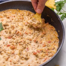 Chip scooping Rotel tomato dip out of black skillet.