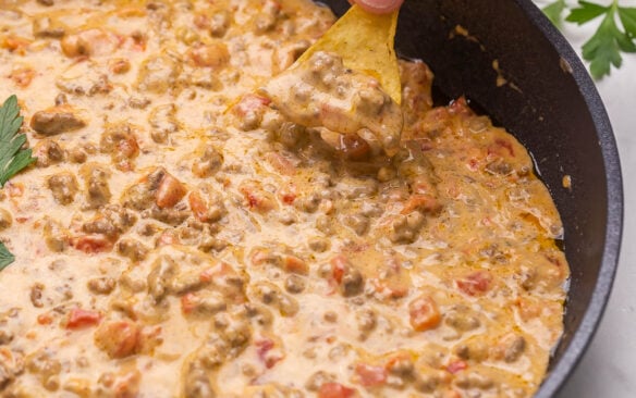 Chip scooping Rotel tomato dip out of black skillet.