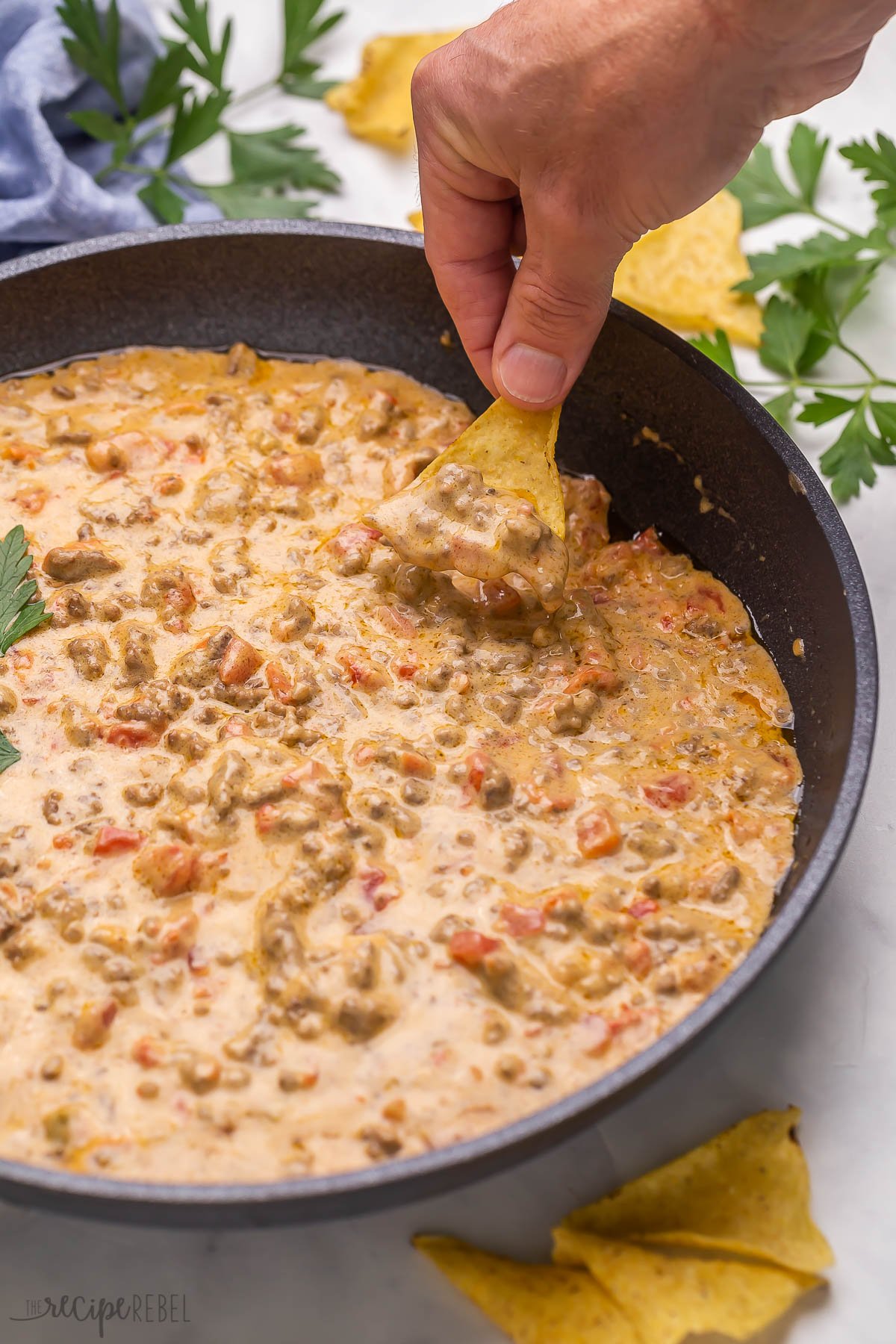 Chip scooping Rotel tomato dip out of black skillet.