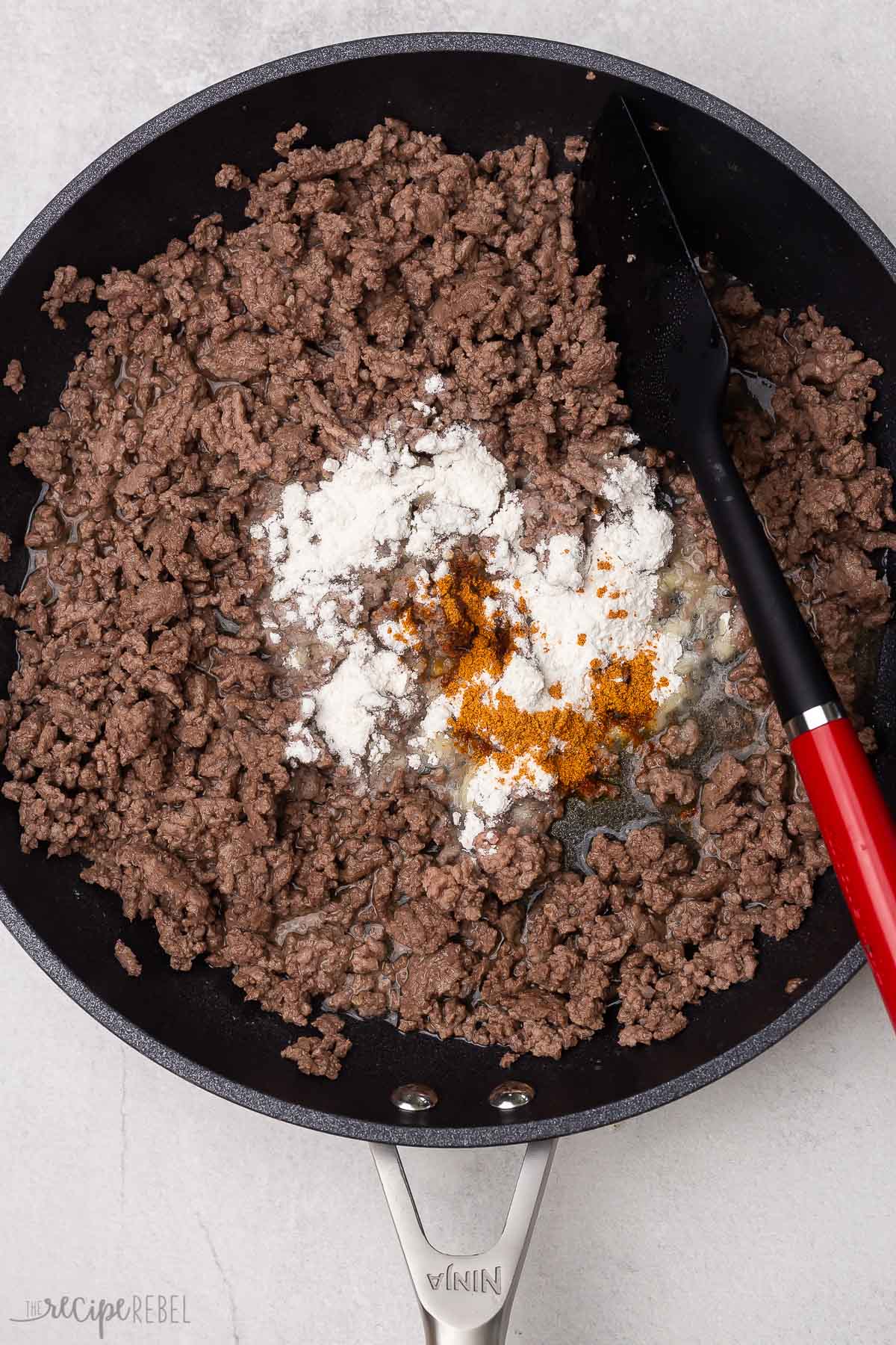 ground beef cooked in black skillet with seasoning and flour added.