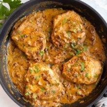 four smothered pork chops in black skillet with sauce.