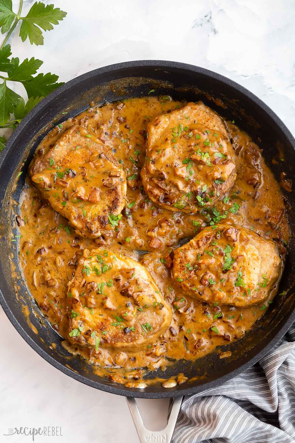 four smothered pork chops in black skillet with sauce.