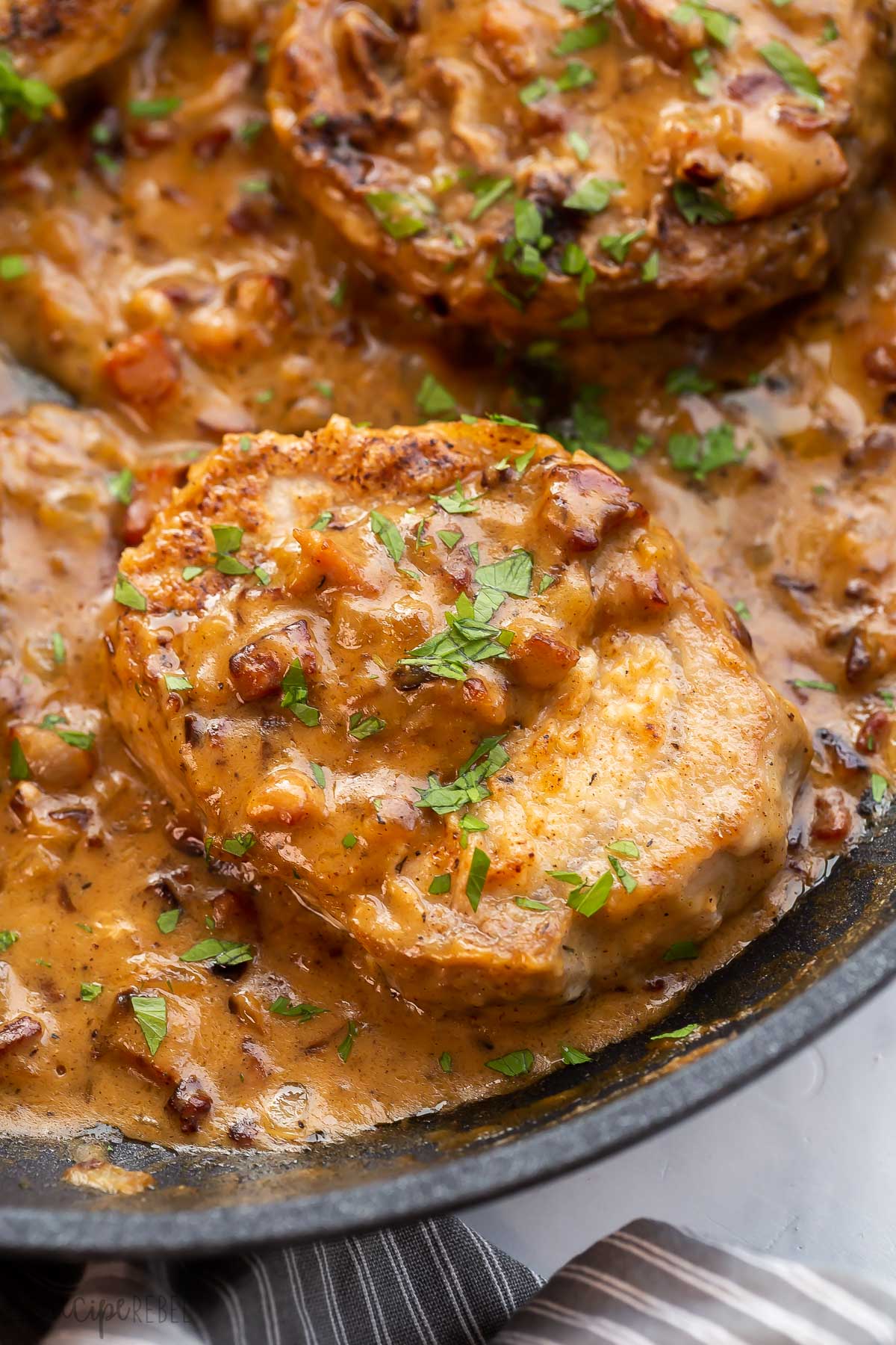 close up image of one pork chop with gravy and bacon.