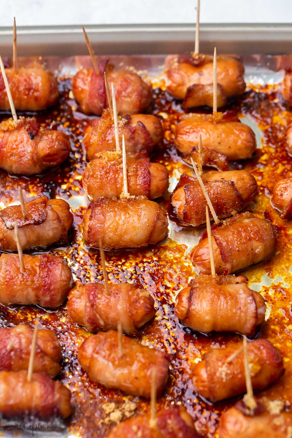 close up image of bacon wrapped smokies on pan.