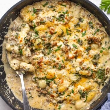 overhead image of baked gnocchi with sausage in a black skillet with spoon stuck in.