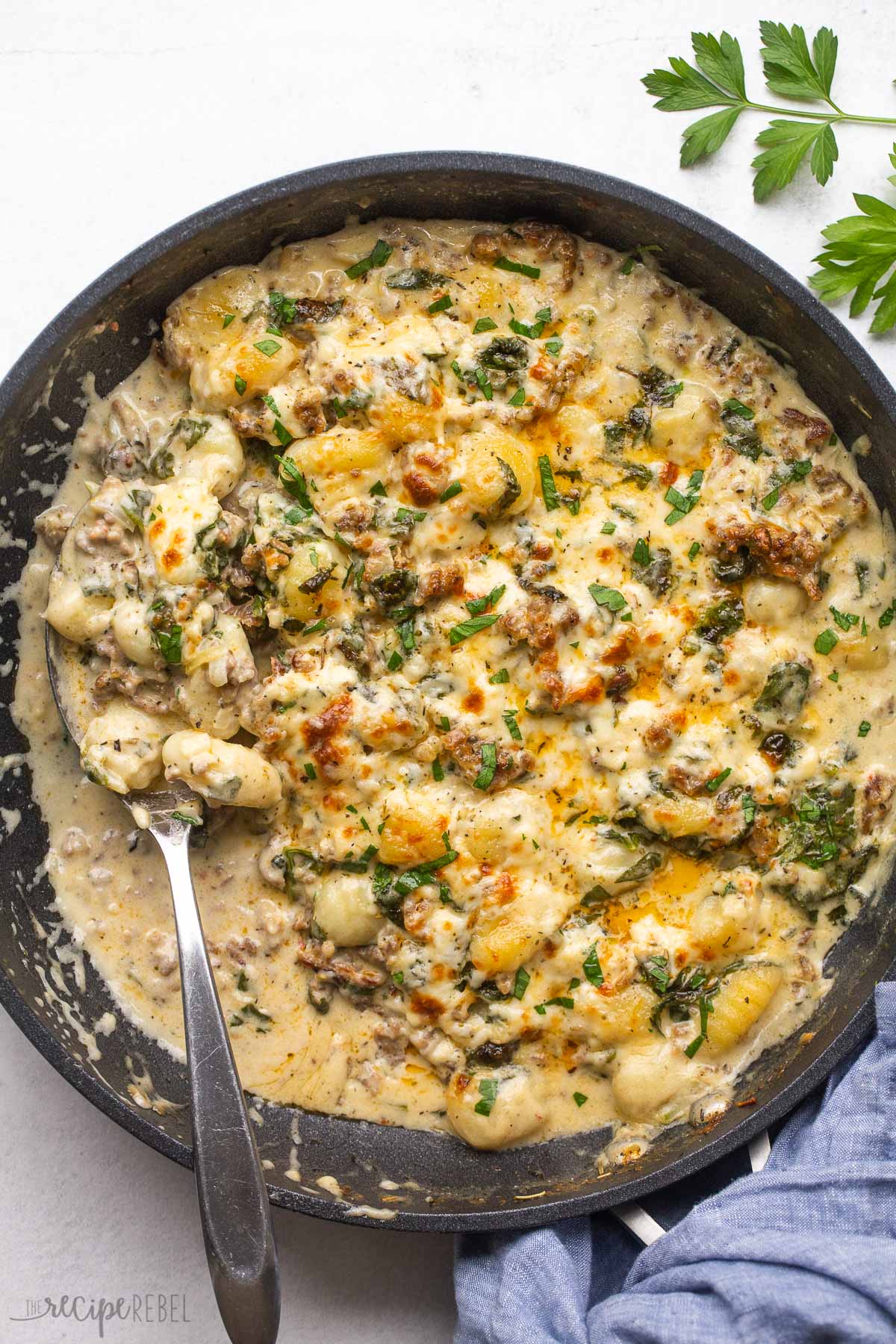 overhead image of baked gnocchi with sausage in a black skillet with spoon stuck in.