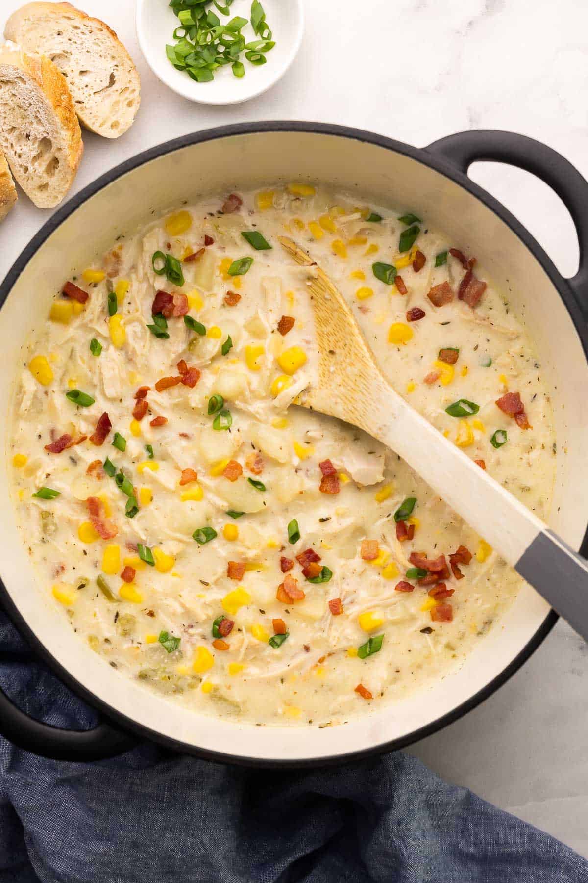 overhead image of chicken corn chowder in a dutch oven with wooden spoon.
