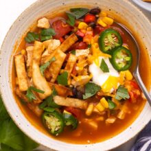 close up image of a bowl of chicken tortilla soup with spoon stuck in.