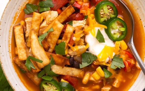 close up image of a bowl of chicken tortilla soup with spoon stuck in.