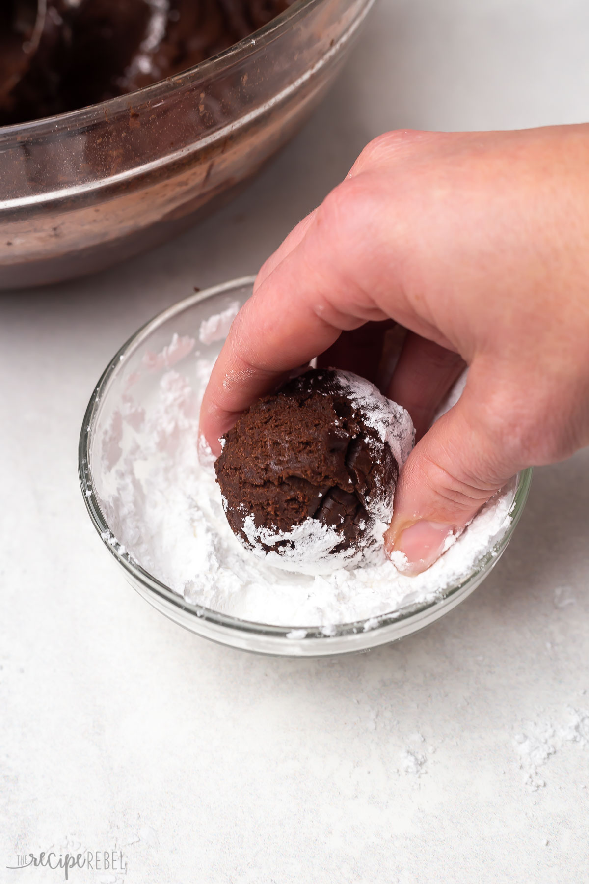 chocolate cookie dough being rolled in powdered sugar.