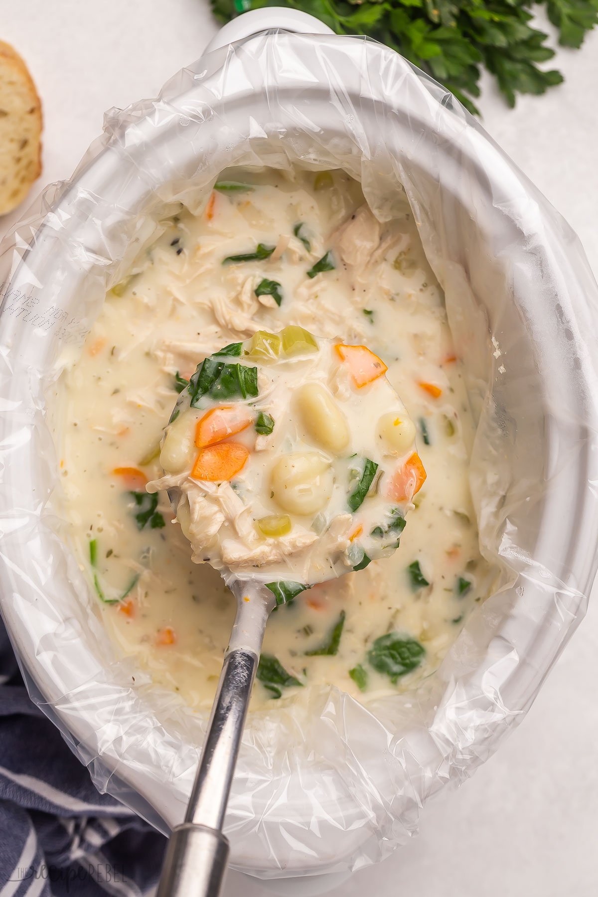 This Slow Cooker Chicken Gnocchi Soup is thick and creamy! Made with tender chicken breasts, vegetables, gnocchi, spinach and Parmesan in a rich and flavorful broth. Perfect with some crusty bread! #soup #slowcooker | slow cooker recipes | crockpot meals | crock pot soup | soup recipes | chicken soup | slow cooker soup | easy dinner ideas metal ladle scooping chicken gnocchi soup out of slow cooker.