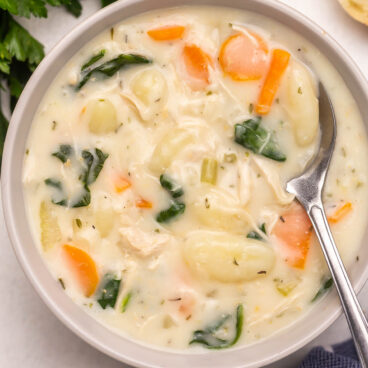 close up image of chicken gnocchi soup in bowl with spoon.